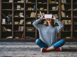 Happy woman wearing VR Glasses in front of bookshelves